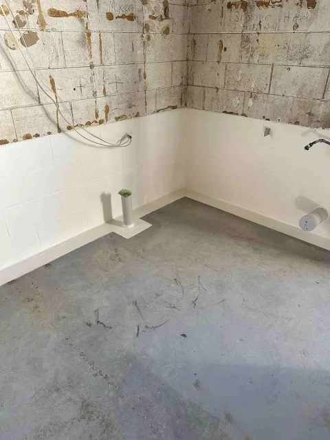 Waterproofed basement corner with sump pump outlet showing tanking applied to concrete block walls